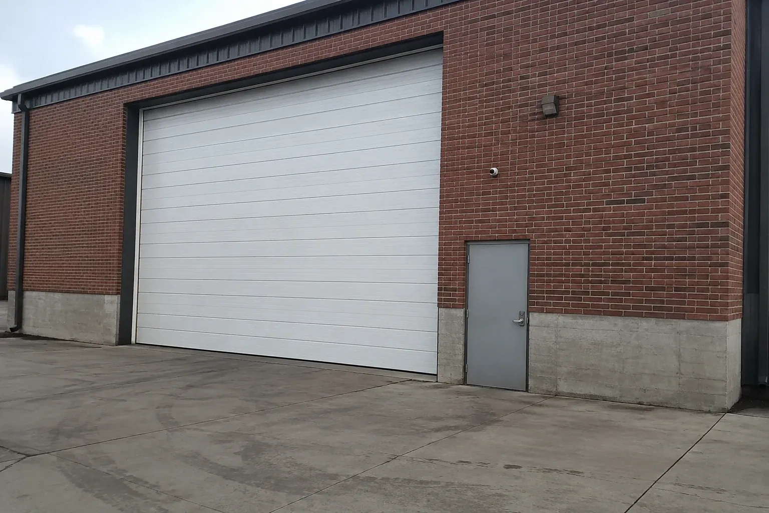 Tall closed sectional loading door beside a personnel door at a brick unit. — Commercial Sectional Door Repair, Collingwood
